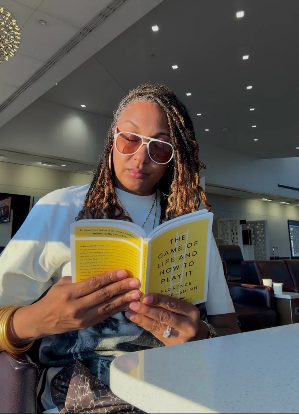 Nalani York in an airport lounge reading a yellow copy of The Game of Life and How to Play It.